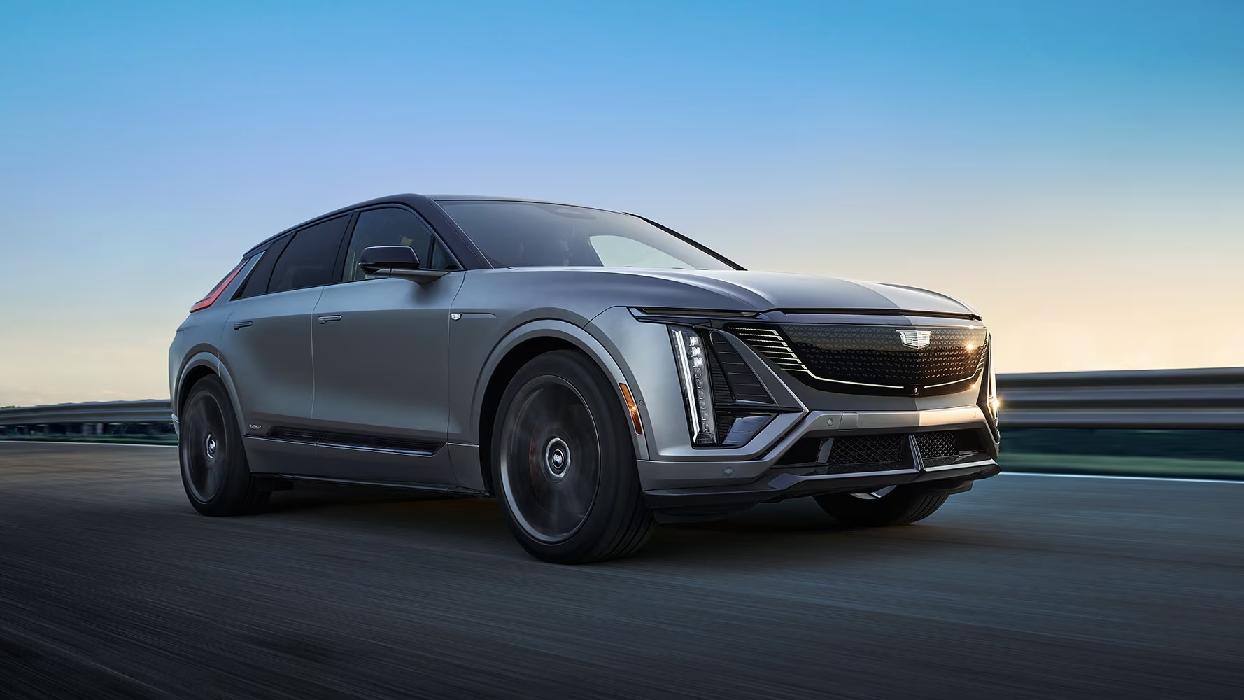Front 3/4 view of the Cadillac Lyriq-V 2026 on the road at sunrise.