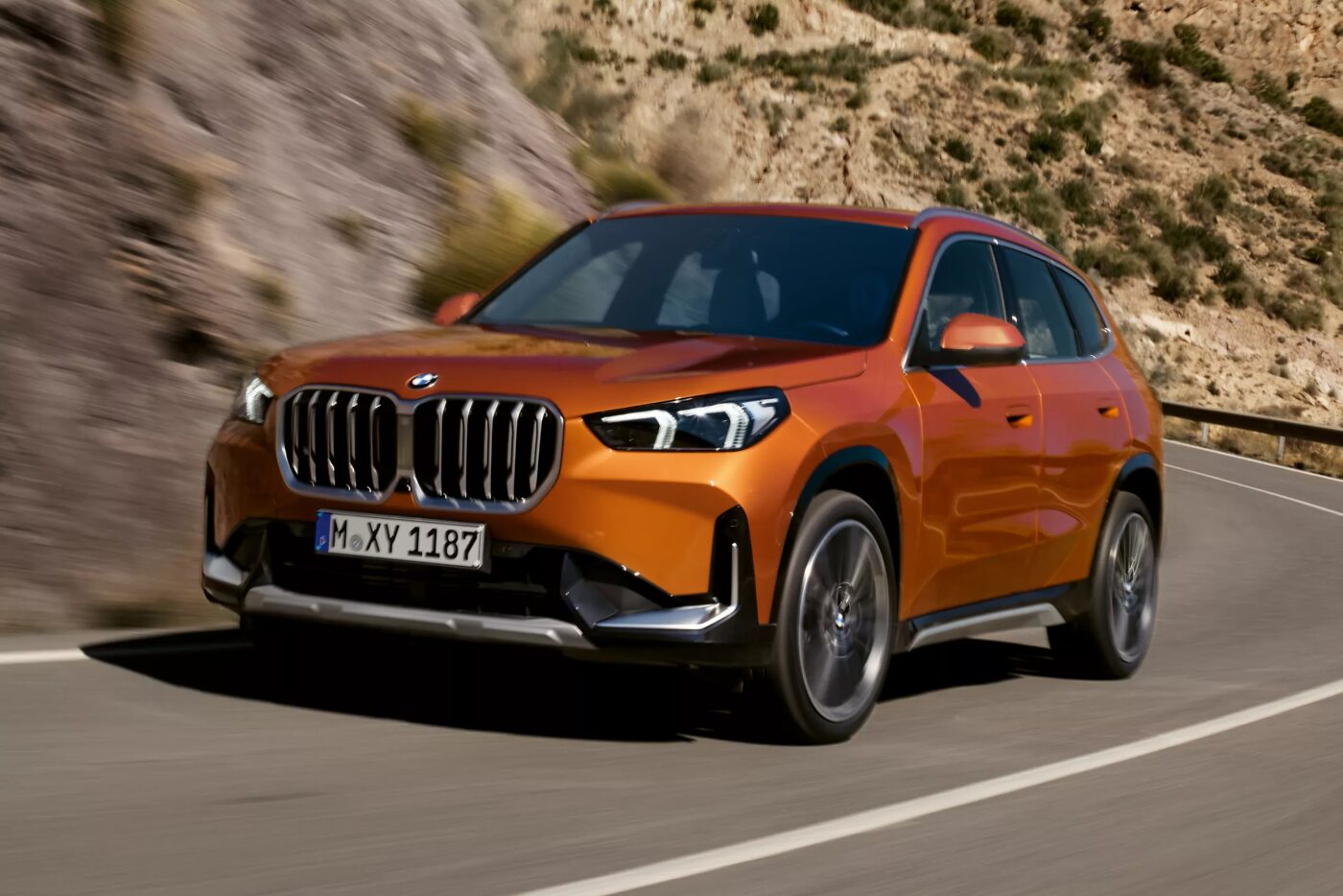 Orange 2025 BMW X1, luxury compact SUV on mountain road.