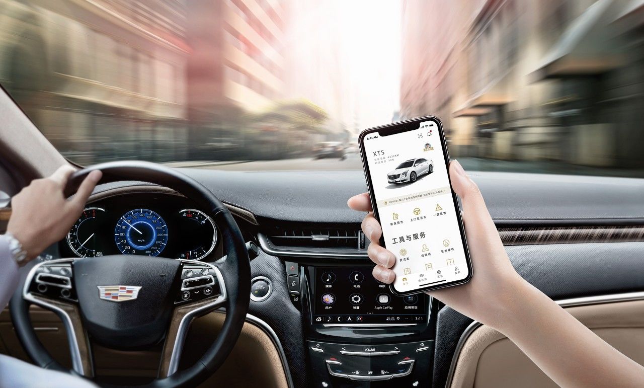 vue d'un couple au volant d'une Cadillac XTS avec son passager qui consulte l'application MyCadillac